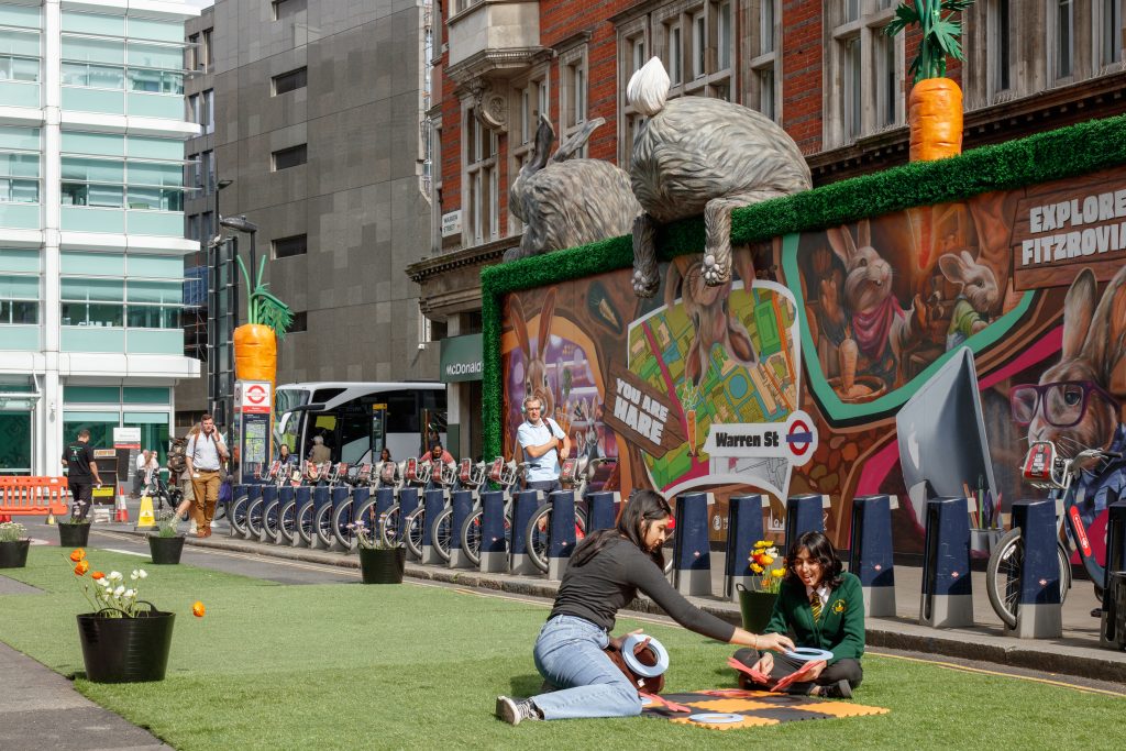 Two people playing a game on the grassed street with rabbit sculptures in background