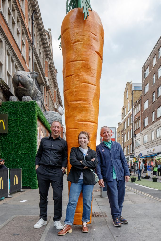 A shot of the team standing in front of a carrot sculpture